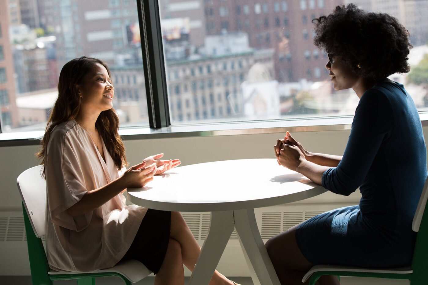 Two people talking across a table, a city skyline behind them