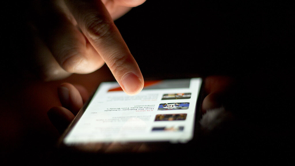 A hand scrolling a smartphone screen in a dark room
