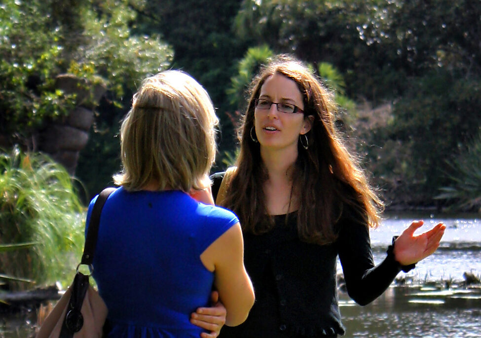 Two women sitting across from each other in conversation, leaning in