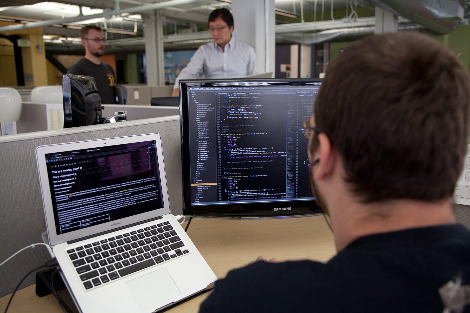A developer working at dual monitors with headphones — the kind of quiet engineering work behind training a neural network on a friend's text messages