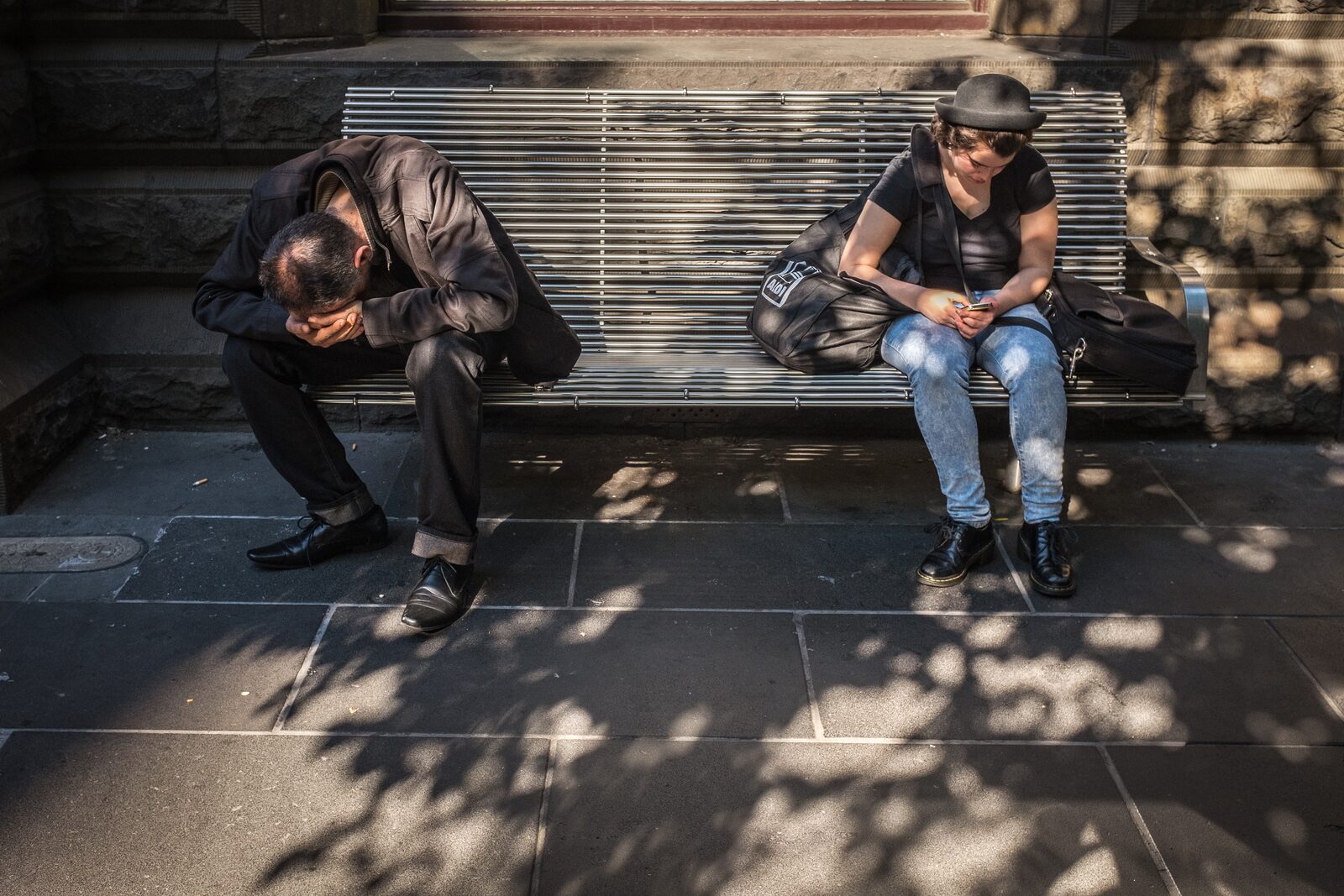 Two people sitting on a bench, both absorbed in their own phones — physical proximity, emotional distance