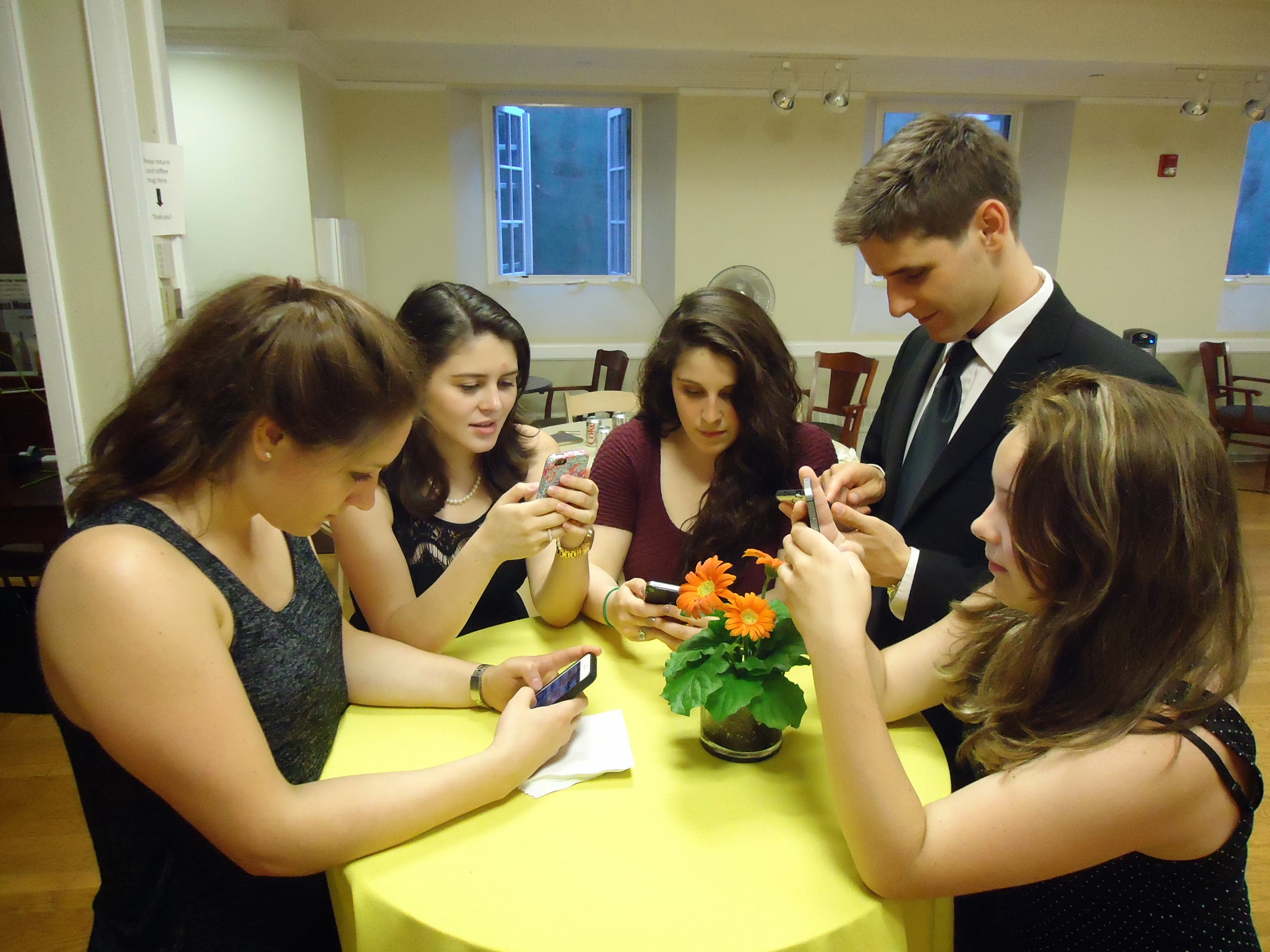 A group of young people at a party, each looking down at their own smartphone screen