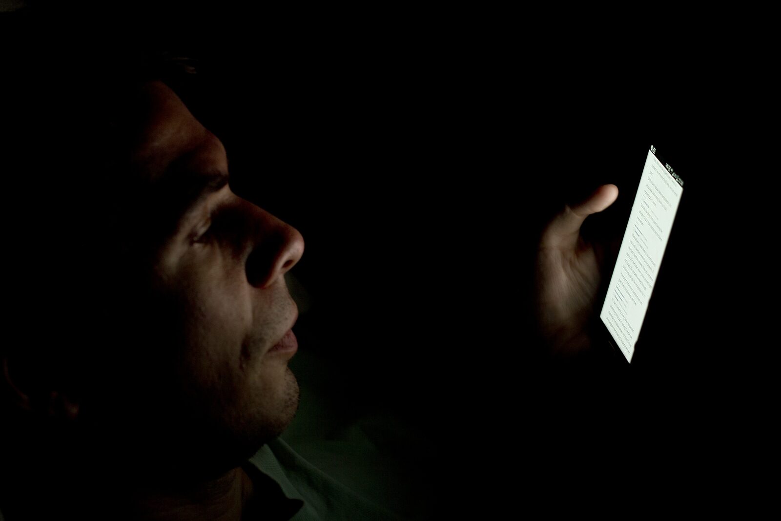 A person's face lit only by their phone screen in a dark room — the late-night intimacy of digital companionship