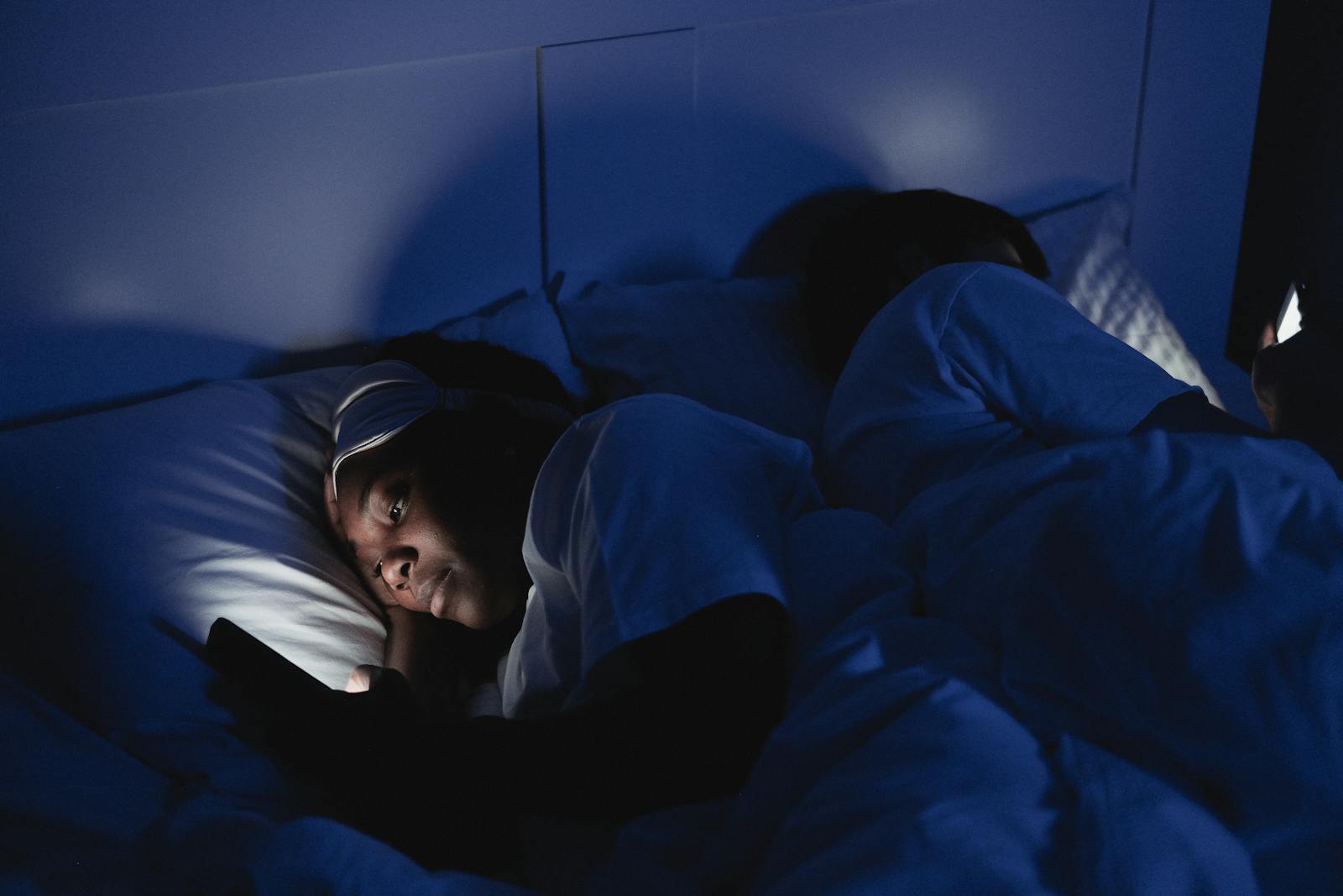 A person in bed at night, face lit by the soft glow of a phone screen — the quiet, intimate context where most AI conversations actually happen
